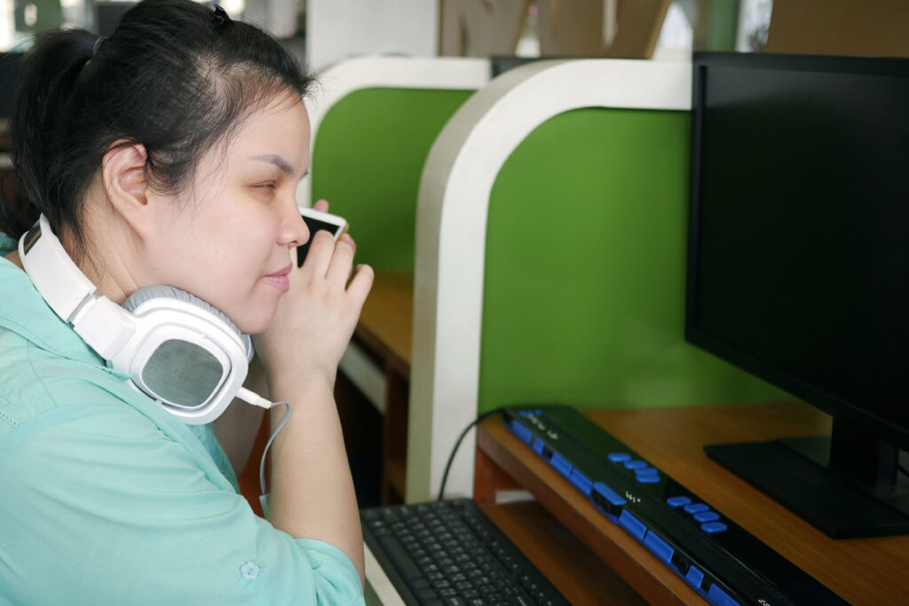 assistive technology blind woman with headphone using computer with refreshable braille display